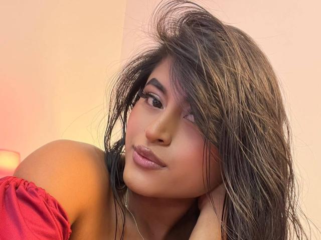MichelleNarvaez has wet, dark brown hair covering one eye, wearing a red off-shoulder top, with glossy pink lips and hoop earrings, looking to the side with a slight smile.