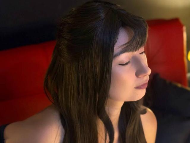 AlessiaLouren hat dunkles, glattes Haar, geschlossene Augen und helle Haut. Sie trägt ein schwarzes Oberteil, und ihr Kopf ist leicht nach rechts geneigt, in einem weichen, warmen Licht..