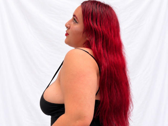 ChoeStar has red hair, black tank top, and visible tits. She's facing side, looking forward, with a nose ring. She's a chubby, fair-skinned woman.