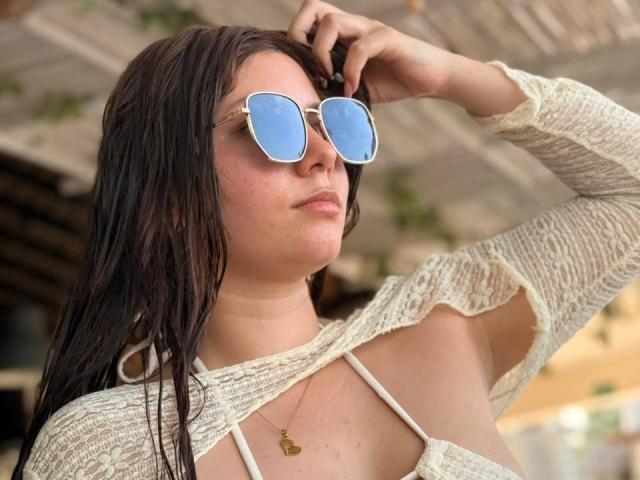 LinaFoxyHot with wet brown hair, wearing blue mirror sunglasses, a white lace top with cutouts, and a gold necklace, touching her hair.