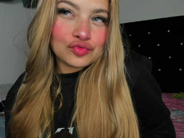 ShantalSummer has blonde hair, pink blush, and puffy pink lips. She's making a pouty face, wearing a black shirt. Her tits aren't visible, just her face and top.