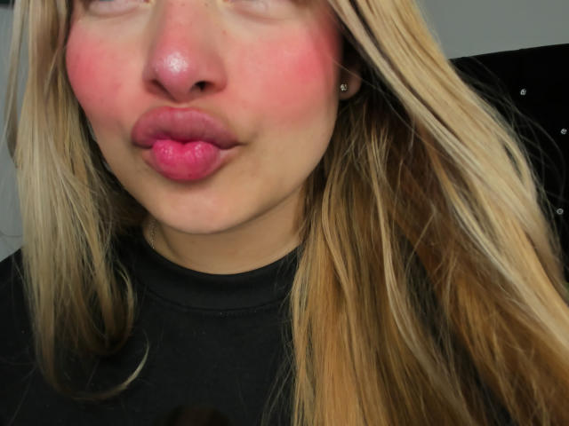 ShantalSummer with pink puffy cheeks, glossy pink lips, and blonde hair, pouting her full ass-like lips. She's wearing a black shirt, and has small earrings.