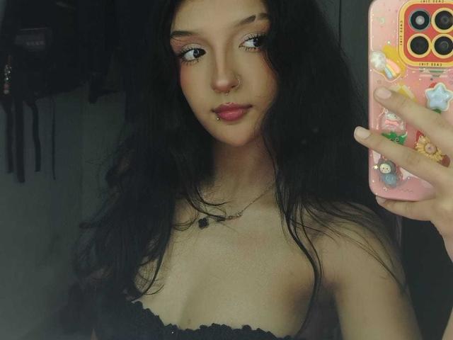 PaulineRey with dark wavy hair, nose ring, and lip piercing, holding a pink phone with stickers, wearing a black strapless top, showing her tits in a mirror selfie.