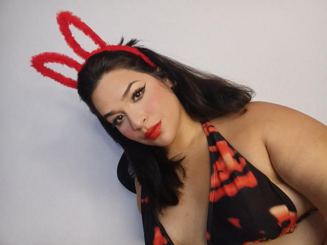 AntonelaPark with red bunny ears, wearing a black and red tie-dye bikini, has red lipstick, and dark hair, looking seductively at the camera with her tits showing.