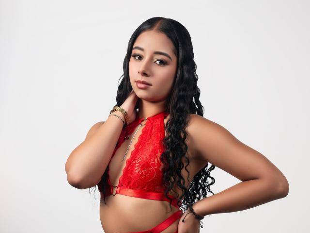 VioletCasandra with long black wavy hair, red lace bralette, tan skin, looking at camera, hand on neck, gold bracelets, confident expression, small tits, slim, sexy.