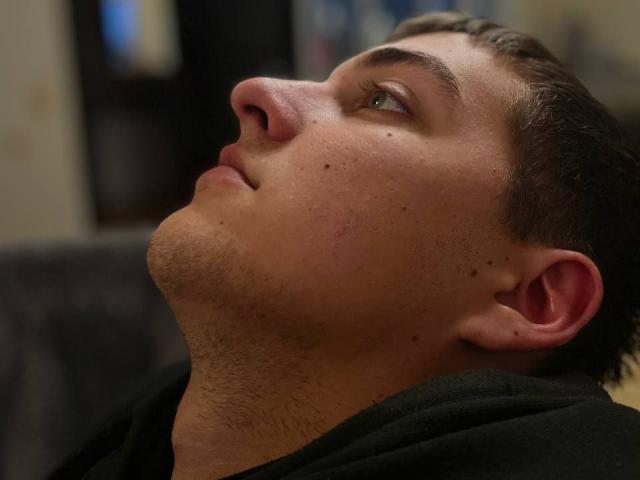 MisterHardcore's face in profile, nose up, eyes looking upward, short brown hair, light skin, small moles, slight stubble, wearing a black hoodie, head slightly tilted back.