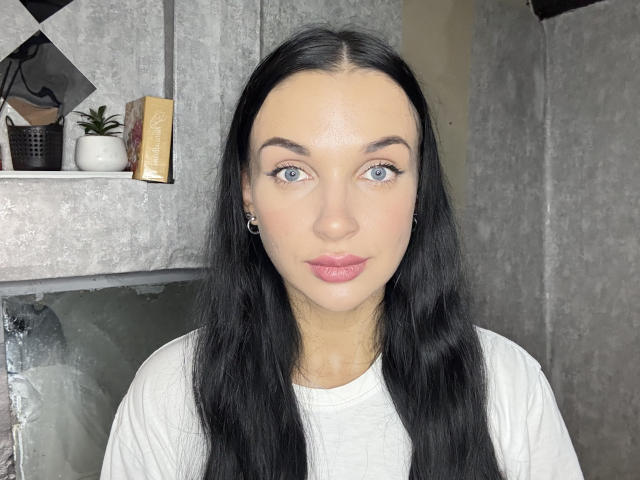 SerenaGlowinski heeft lang zwart haar, blauwe ogen en roze lippen. Ze draagt een witte blouse en heeft kleine oorbellen. Haar gezicht is in het midden geplaatst en ze kijkt recht in de camera..