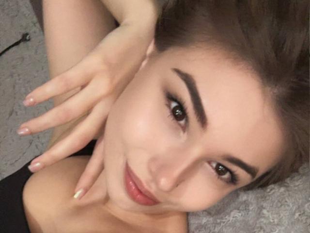 Pearline Berggren hat braune Augen, hochgezogene Augenbrauen und ein leichtes Lächeln, wobei eine Hand ihre Wange berührt. Sie hat glänzende, rosafarbene Lippen, ein schwarzes Oberteil und helle Haut..