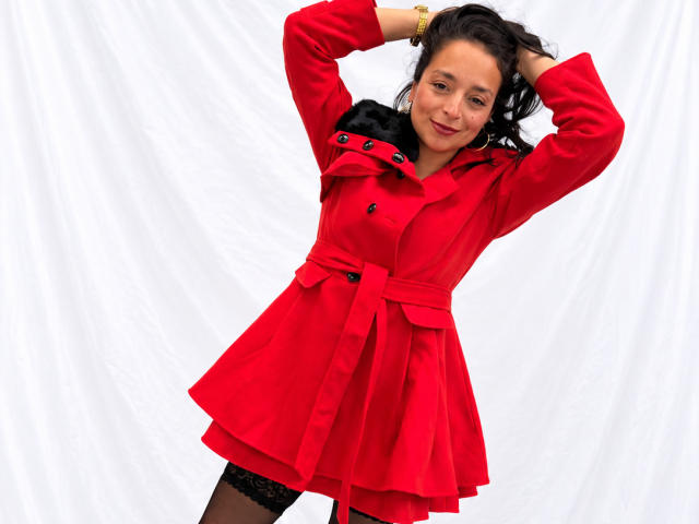 StangelarRivera, red dress, black lace stockings, arms raised, smiling, hands in black hair, red belt, black buttons, white background, red lipstick, brunette, medium tits, cute, confident.