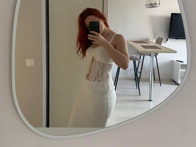 ErnestinaMcintrye with red hair, wearing a white lace dress, holding a green phone, taking a mirror selfie, showing her tits and ass.