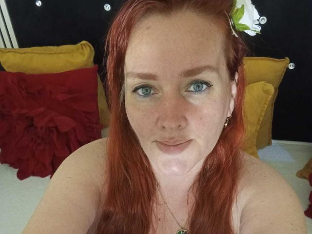 SinFulTitsDD ha i capelli rossi, gli occhi azzurri e delle lentiggini, con un leggero sorriso e senza vestiti, indossa una piccola collana d'oro e guarda direttamente la fotocamera..