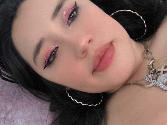 JessyBarnnett's face with pink eyeliner, black eyelashes, full pink lips, black hair, silver hoop earrings, and a necklace with a cute pendant. Her ass is not visible.