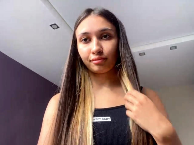 Brenda Bovia mit langem, braun-blondem Haar, die einen Schlüssel hält, trägt ein schwarzes, geripptes Tanktop, hat braune Augen und ein leichtes Lächeln, in einem schlichten Innenraum..
