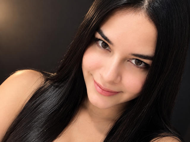 AuroraSantorini has long black hair, brown eyes, and a slight smile. She's looking at the camera with a cute, innocent expression and a smooth, fair skin tone.