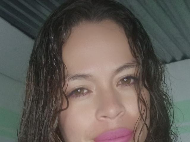 Sandytatiana hat feuchtes, braunes Haar, braune Augen und rosafarbenen Lippenstift und blickt direkt in die Kamera mit einem neutralen Ausdruck. Ihr Gesicht ist im Bild zentriert..