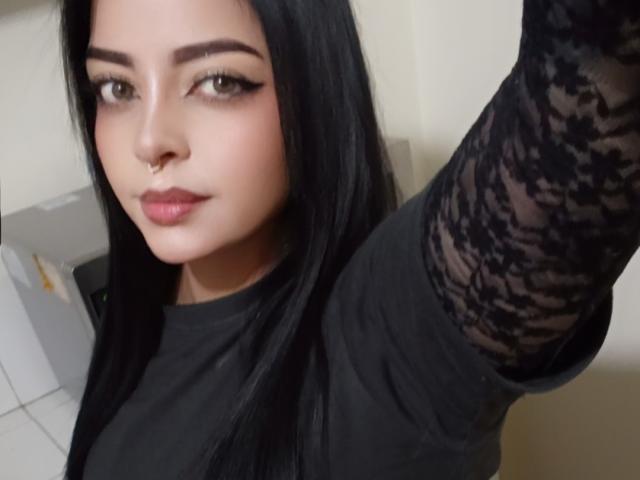 LilithAmoth has long black hair, a nose ring, and wears a black lace-sleeve top, looking at the camera with winged eyeliner and pink lipstick.