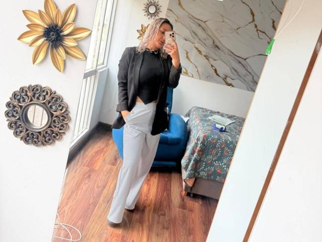 ElenaSaenz stands in a mirror selfie, wearing a black top, black blazer, gray pants, and brown heels, with hands in pockets, showing her ass in a modern room.