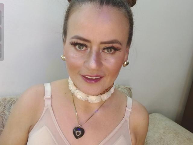 Maghentaa, avec ses cheveux bruns attachés en chignons, porte un soutien-gorge rose, un collier de perles blanches et des boucles d'oreilles dorées. Elle a les yeux bleus, de longs cils et du rouge à lèvres rose. Ses seins sont visibles..