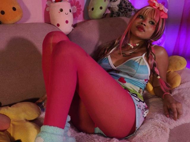 LiMiuu with pink tights, blue tank top, white shorts, pink hair, and pink bow, sitting on a pink couch, showing her tits and ass, surrounded by stuffed animals.