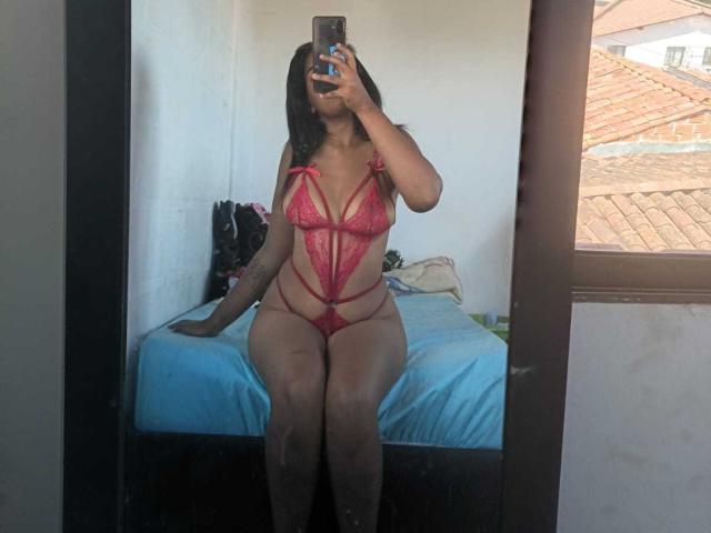 MiaStClaire with dark hair, wearing red lace lingerie, showing big tits and thick ass, sitting on bed, taking mirror selfie, holding phone. Bedroom with window.