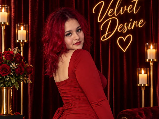 RosalieVittoria with red curly hair, wearing a red dress, looking over her shoulder, showing her tits, standing in front of candles and red roses, smiling.