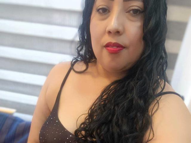 AmberMoretti with wet black hair, red lipstick, and a brown polka-dot top, showing her tits in a selfie. Her eyes are half-open, and she has a slight smile.