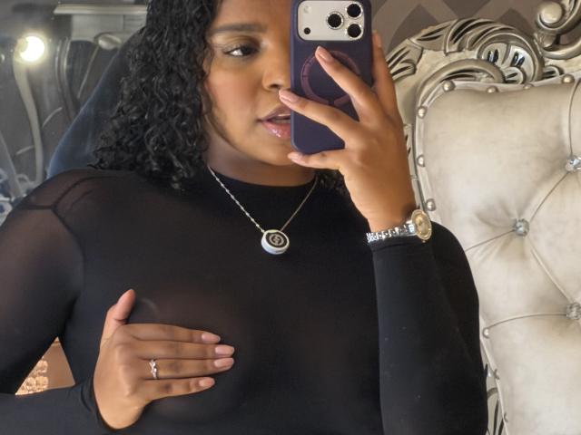 LisaMendez with curly black hair, wearing a sheer black top, covering her small tits with her hand, taking a mirror selfie with her phone, wearing a necklace and watch.