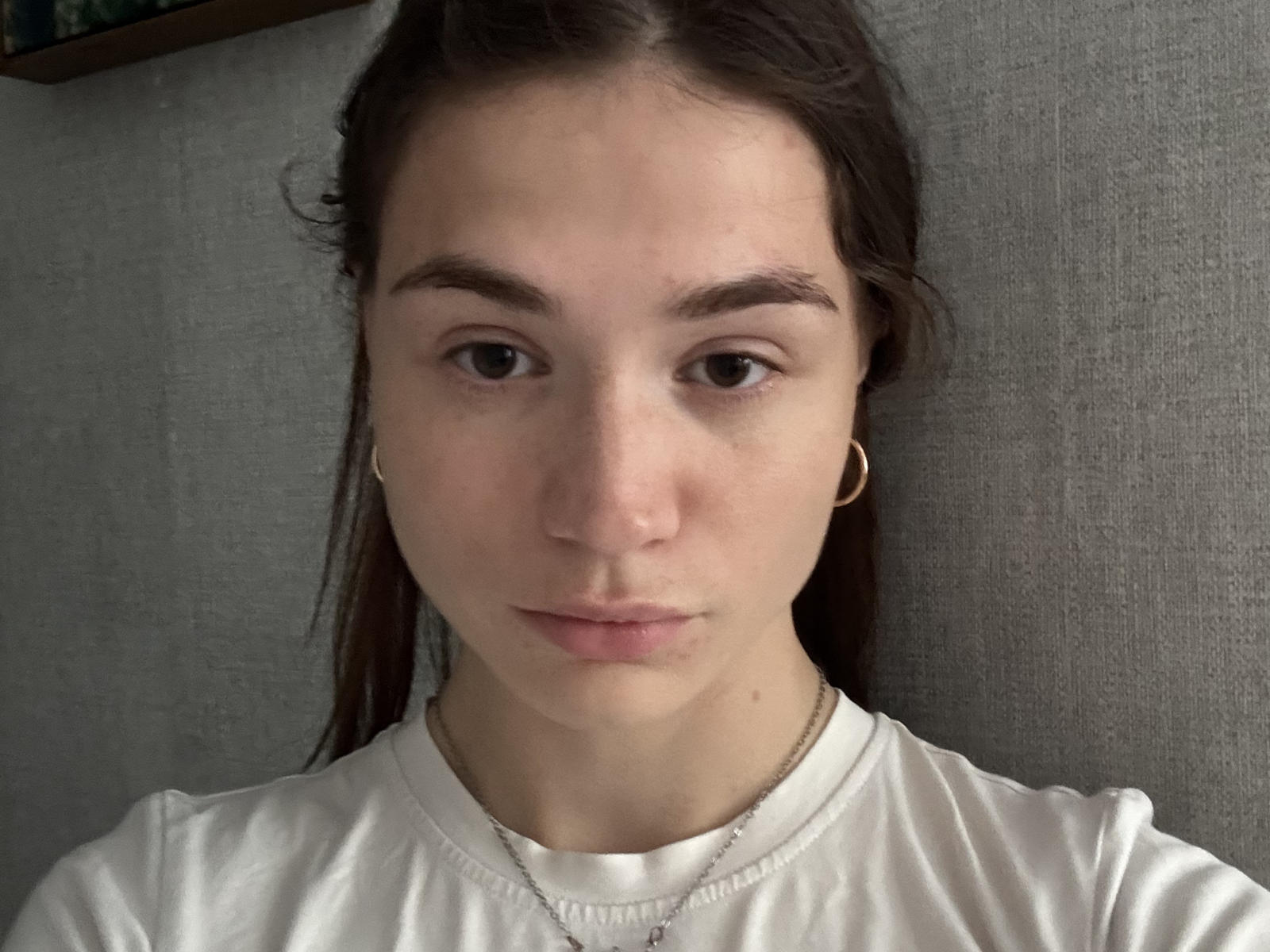 Shelley Vangompel ha un'espressione neutra, la pelle chiara, gli occhi marroni e i capelli lunghi e scuri, indossa una camicia bianca e piccoli orecchini a cerchio dorati, con una sottile collana..