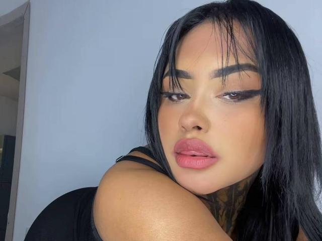LairaHearvy has black hair, full pink lips, and tattoos on her neck. She's wearing black with thick eyeliner and a sultry expression. Her boobs are slightly visible.