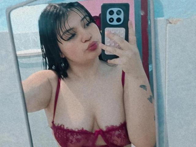 MackenHott with wet black hair, red lace bra, pouty lips, holding phone, showing big tits, tattoo on arm, taking mirror selfie.