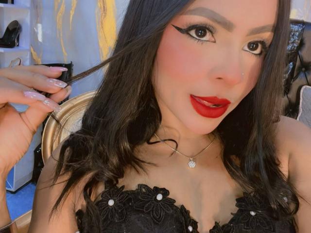 LindaFrancoo has dark hair, red lipstick, and black eyeliner, wearing a black lace top with flower details, showing off her tits and a cute nose ring.