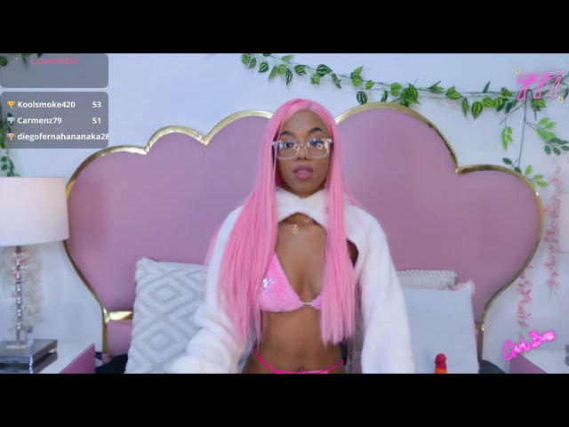 AllisonRomano with pink hair, glasses, white fur jacket, pink bra, showing her tits, sitting on pink bed, green leaf vines in background, cute and sexy.