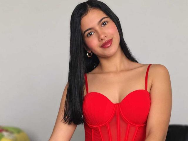 AmilyPreston has dark straight hair, wearing a red bra that shows her small tits, with a slight smile and red lipstick, and small hoop earrings, against a plain background.