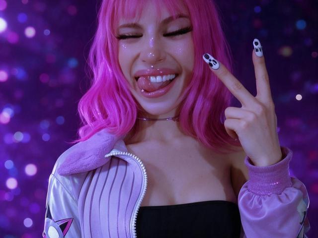 Maaddy69 with pink hair, tongue out, making a rock-n-roll hand gesture, wearing a pink jacket, black tube top, and skull nails, smiling with glitter on her face.