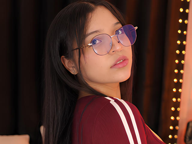 InnocenthaZel with long black hair, wearing round glasses and a red shirt with white stripes, looking over her shoulder, her pink lips slightly parted, soft brown skin, and cute.