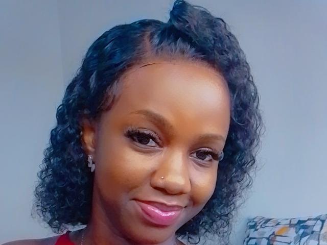 SexyAurora a les cheveux noirs et bouclés, des yeux marron, du rouge à lèvres rose, un piercing au nez et des boucles d'oreilles en diamant, et elle sourit légèrement. Sa peau est lisse et elle a un visage mignon et séduisant..