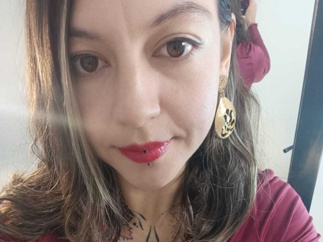 ArianaBlonde tiene piel clara, ojos marrones y cabello ondulado castaño. Lleva lápiz labial rojo, un arete dorado con diseño negro y una blusa roja. Tiene un piercing en el labio..