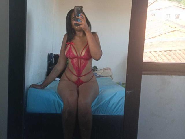 MiaStClaire in red lace lingerie with straps, sitting on a bed, holding a phone, showing her tits and pussy, with black hair and tattoos, in a mirror selfie.