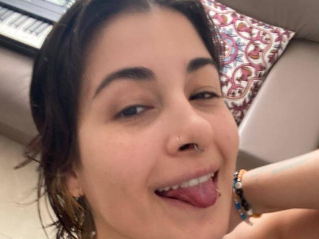 NyxVale has dark brown hair, a nose ring, and is sticking out her tongue with her eyes half-closed. She's smiling, showing her teeth. She's wearing a beaded bracelet.