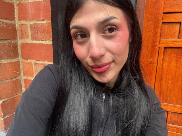 Sophie Beaumont ha i capelli neri, le guance rosate e un piercing carino al naso. Indossa una maglietta nera con una cerniera, e le sue labbra rosa sono leggermente incurvate in un sorriso..