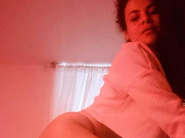 MissSunnyShine with curly hair, wearing a white shirt, showing her ass, looking over her shoulder, red-tinted photo, soft lighting, subtle smile.