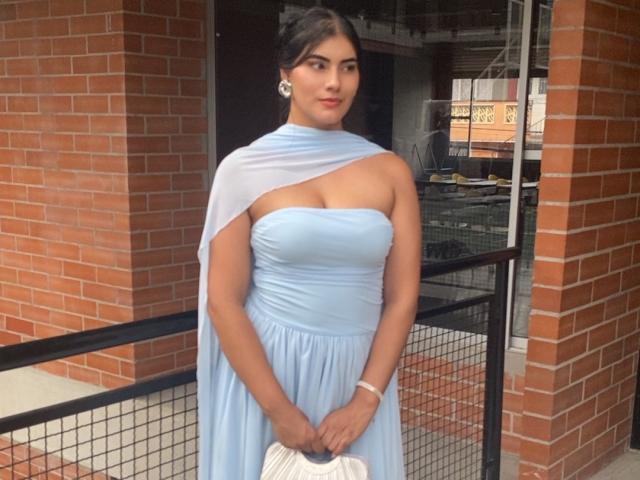 AlaraKey has big tits in a light blue, strapless dress with a white cape, holding a white clutch, standing in front of red brick walls, looking cute.