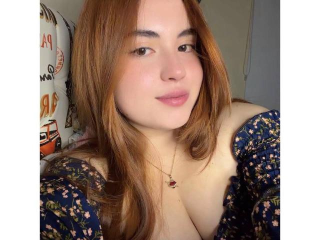 VicluX has light skin, brown hair, and is wearing a blue floral dress with off-shoulder sleeves, showing her cleavage, and a necklace with a red pendant.