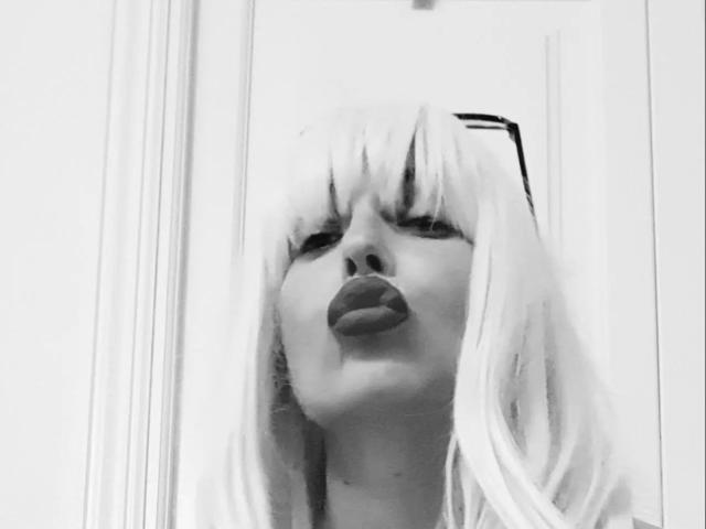 NattyNat-hot with platinum blonde hair, puffy lips, and full makeup, looking up through a glass window, showing off her plump ass reflected in the glass. Black and white.