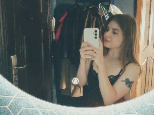 Alysia Fillingham maakt een selfie in een spiegel, gekleed in zwarte kanten lingerie, waarbij haar borsten zichtbaar zijn, met een vlindertatoeage op haar rechterarm, en ze houdt een witte iPhone vast..
