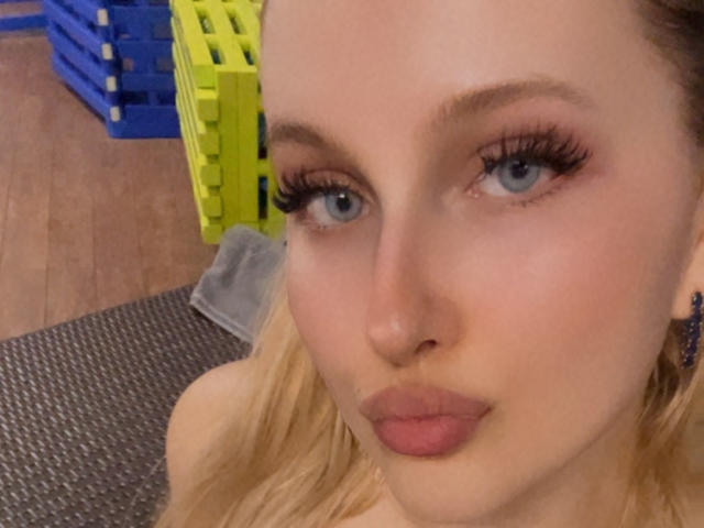 SimonaKorzep's pouty face with blue eyes, long eyelashes, and pink lips. She's got blonde hair, fair skin, and a slightly smug expression. Her tits are not visible.