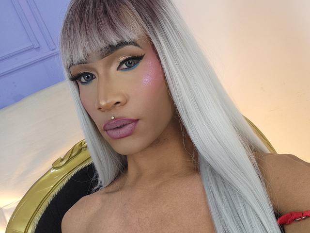 KeyceSex tem cabelos longos e lisos, brancos com pontas loiras, delineador azul, blush rosa e um piercing no nariz. Ela tem lábios rosados e um colar de ouro que mal se vê..
