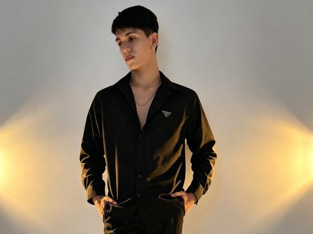 NicolasRosenthal with hands in black shirt pockets, looking to the side, wearing a necklace, short black hair, light skin, and a small logo on the shirt.