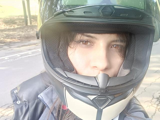 VioletaStone wearing a black and green helmet with a mesh visor, brown eyes, and a slightly pouty expression, showing her nose and upper lips, with her jacket on.