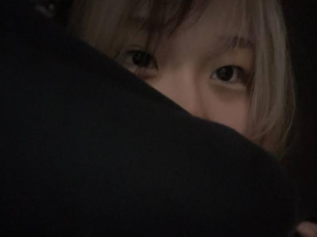 JungMcgranor's face partially hidden, eyes peering over a dark, blurry object. Light brown hair, subtle expression, dark background. JungMcgranor's eyes are focused and slightly curious.